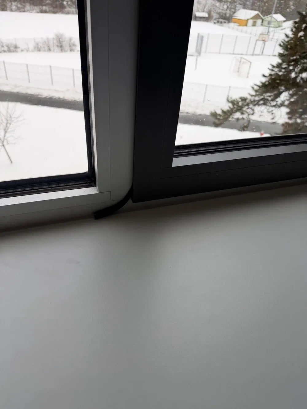 Unterer Rahmen eines Fensters im Winter, eine gelöste Dichtung hängt aus dem Falz, draußen liegt Schnee